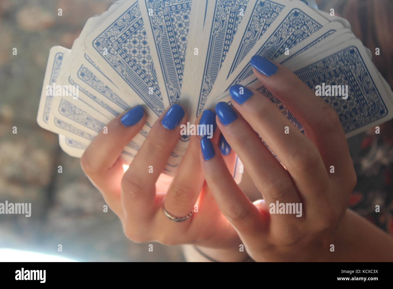 Female hands with blue fingernails spread pack of blue playing cards on wooden table. Stock Photo