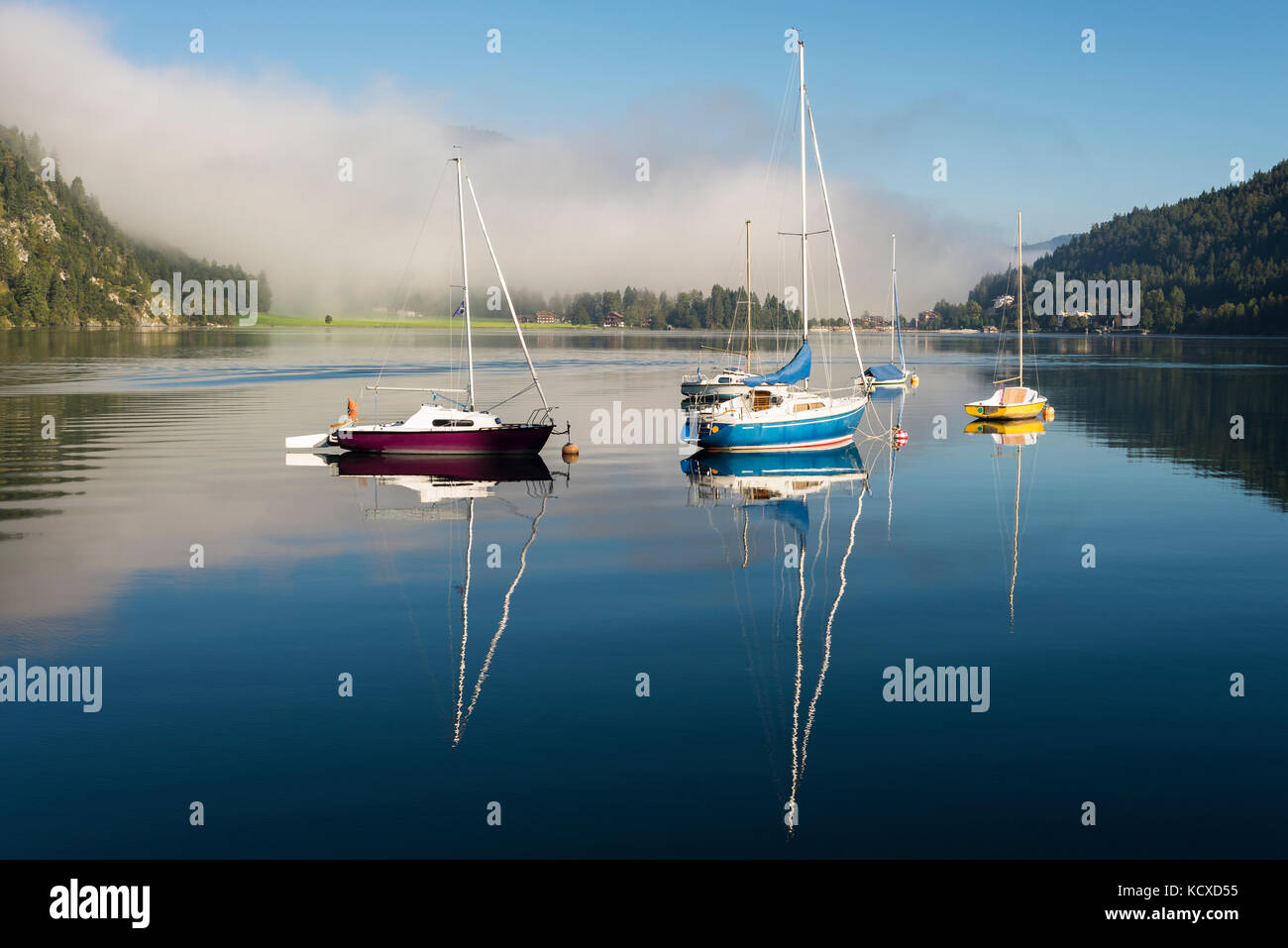 Mist, mountains, sailing boats and yachts in the morning sun reflected in the calm surface of the Lake Achensee in autumn, Tyrol, Austria Stock Photo