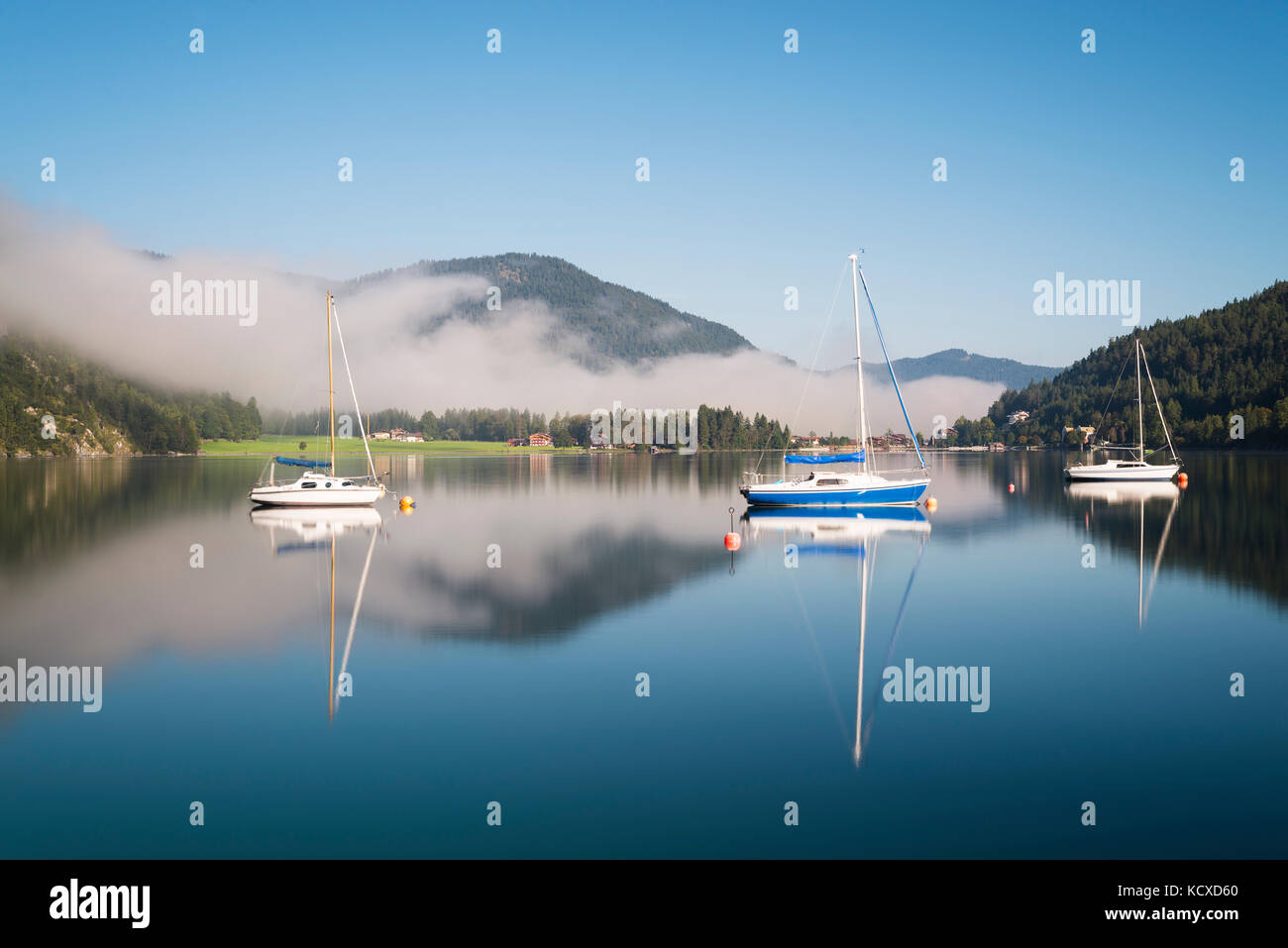 Mist, mountains, sailing boats and yachts in the morning sun reflected in the calm surface of the Lake Achensee in autumn, Tyrol, Austria Stock Photo