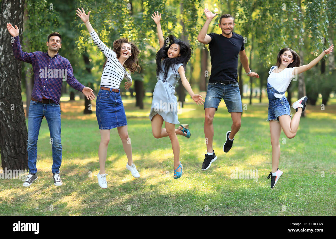 Five happy friends young women and men jumping outdoors. Cheerful people having fun in park on sunny day. Freedom, victory, action, healthy lifestyle  Stock Photo