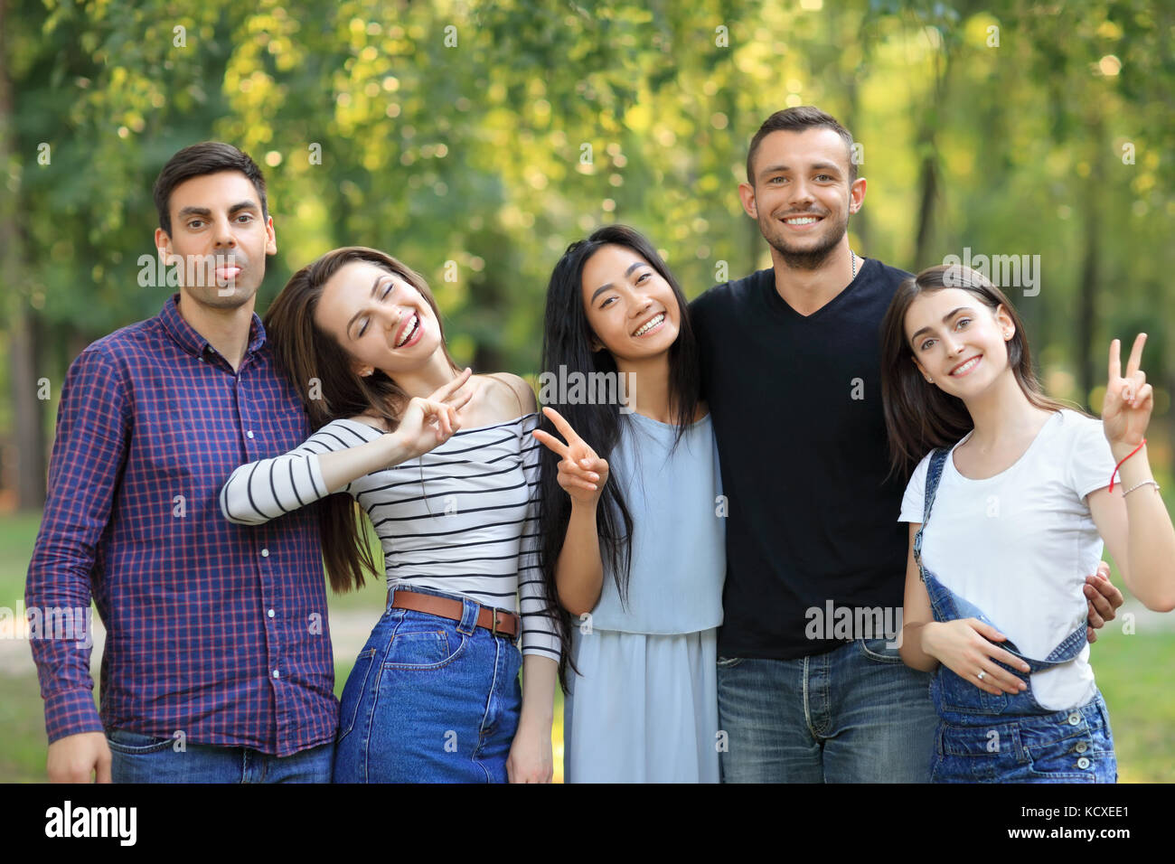 Happy friends men and women with facial expressions and gestures. Young cheerful people showing peace sign and tongue. Guy in black t-shirt expresses  Stock Photo