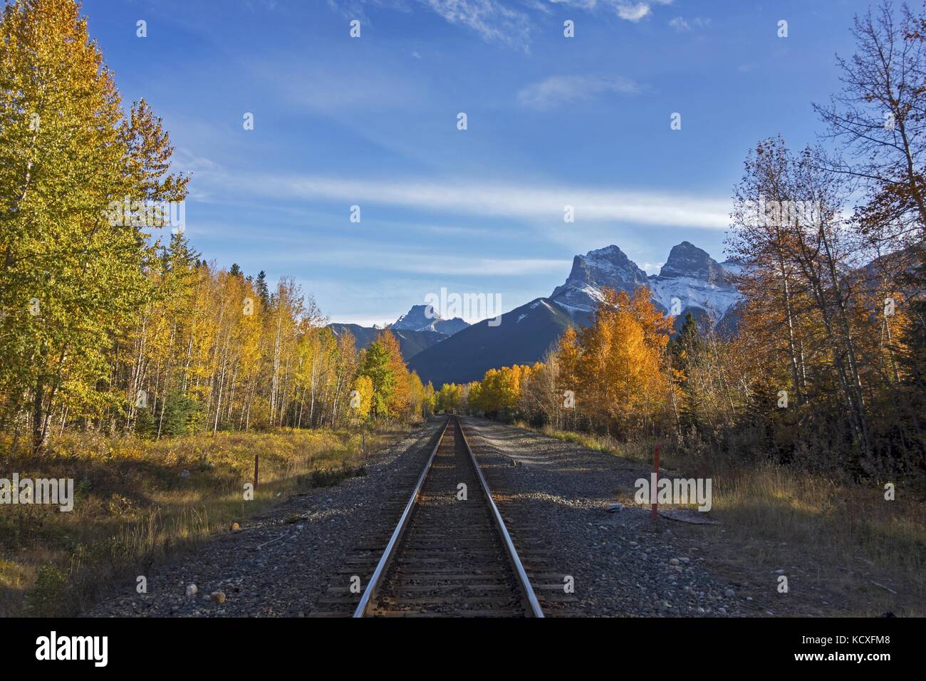 Canadian Pacific Railway Line Crossing near Town of Canmore in Alberta Foothills with Distant Three Sisters Mountain Landscape View Stock Photo