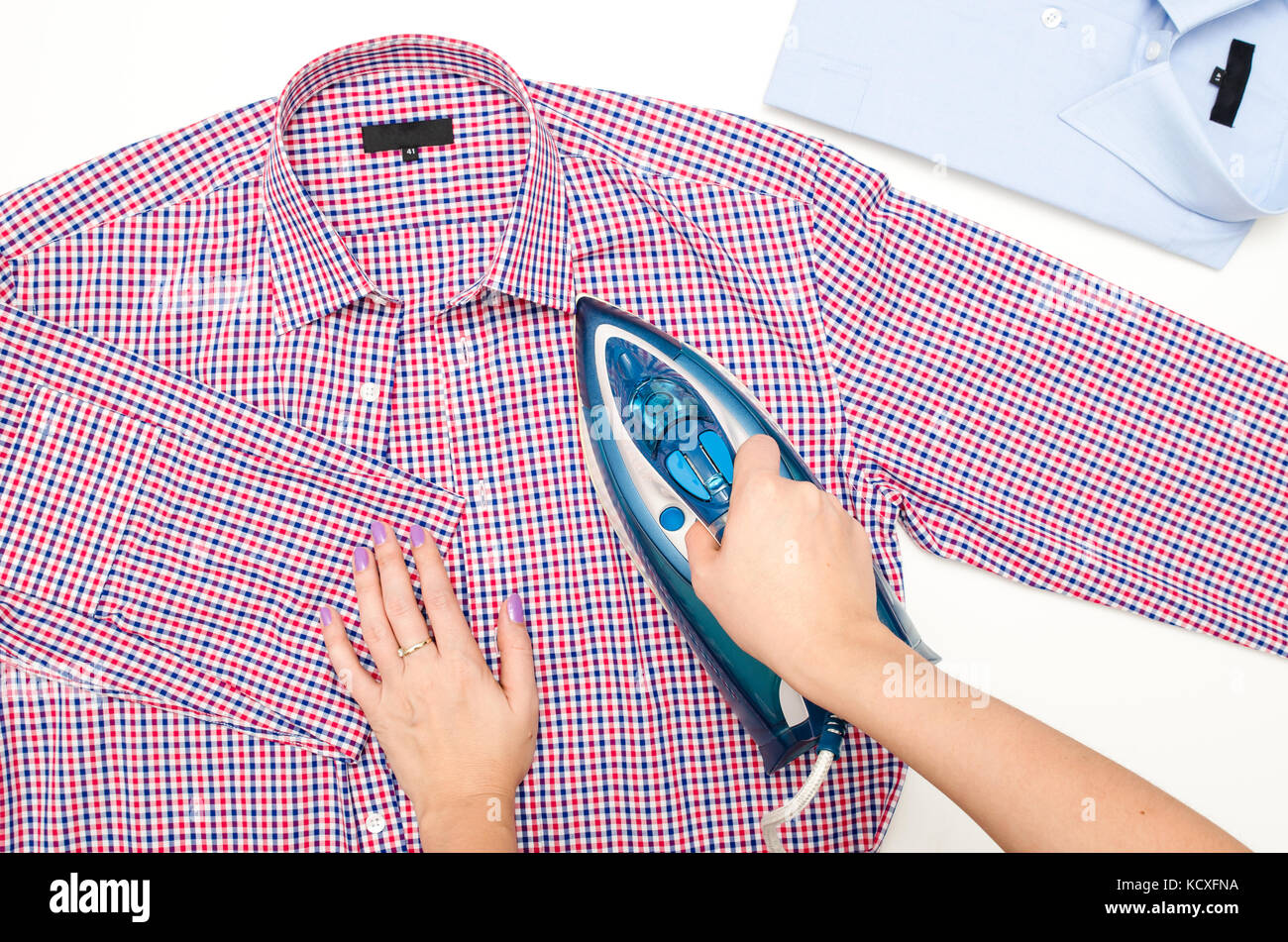 Female hand ironing men's shirt. Blue iron on white background top view