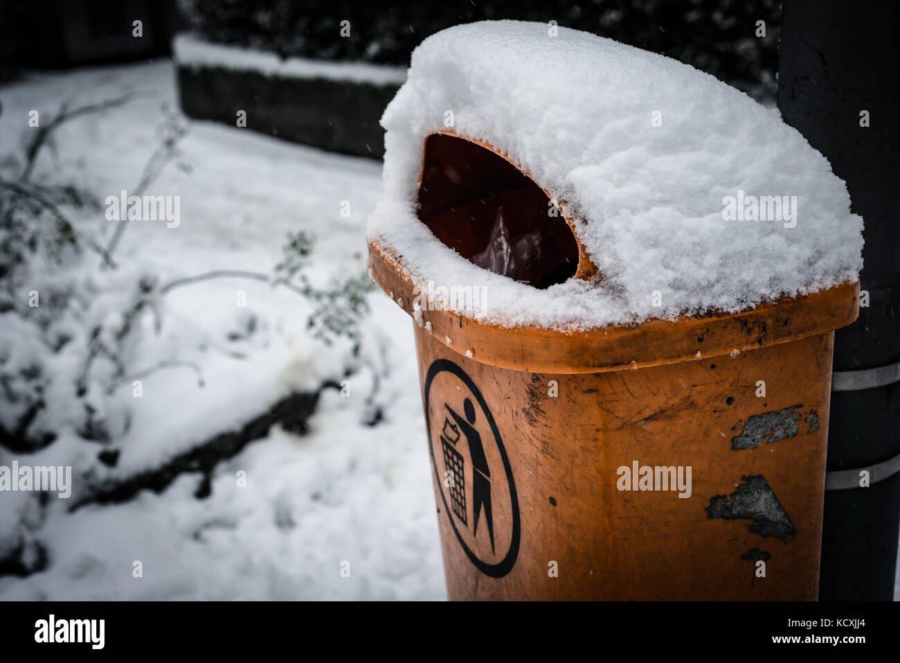 Dirty orange trashcan rubbish dustbin in winter covered with snow Stock Photo