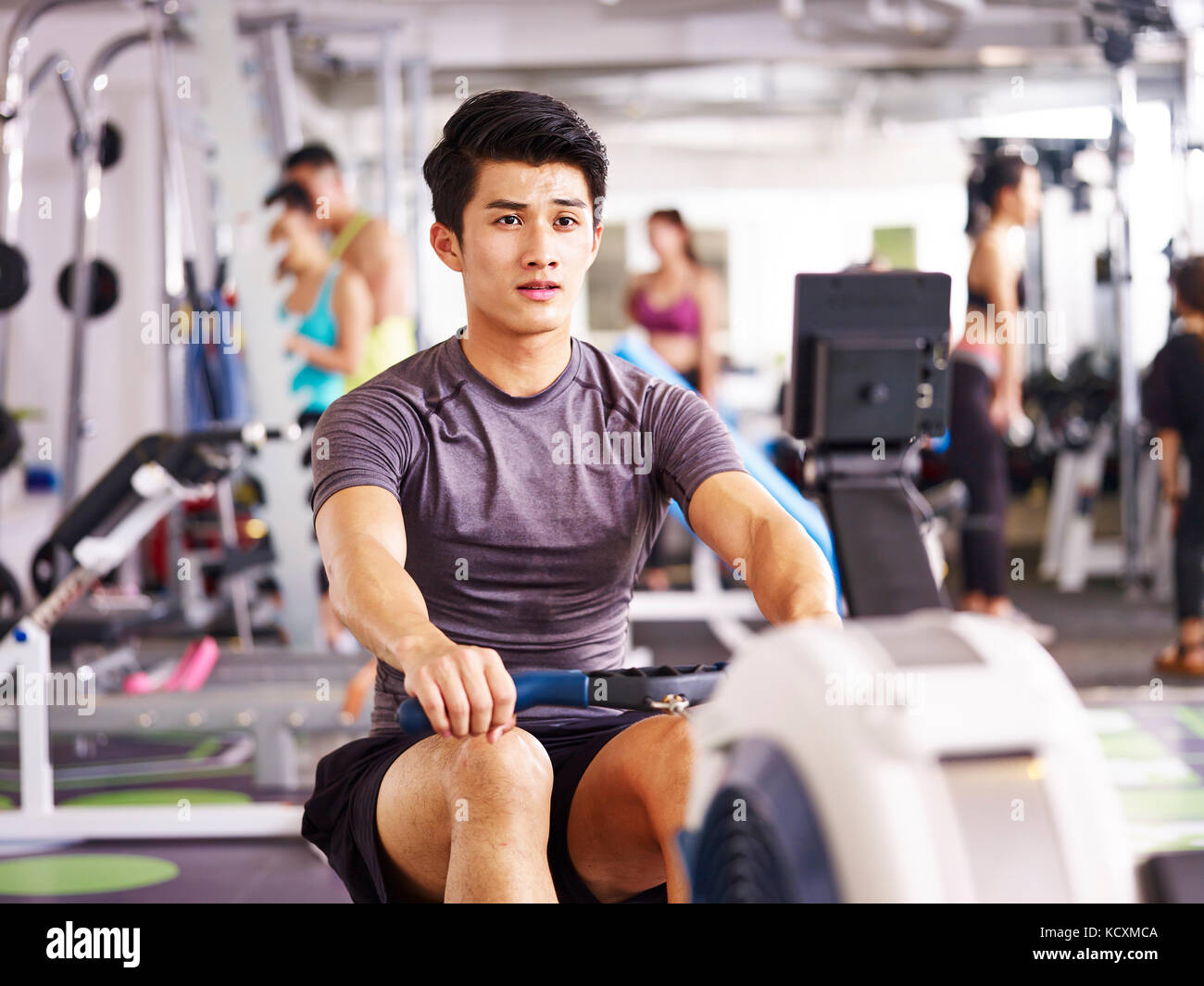 young asian adult man working out in gym using rowing machine. Stock Photo