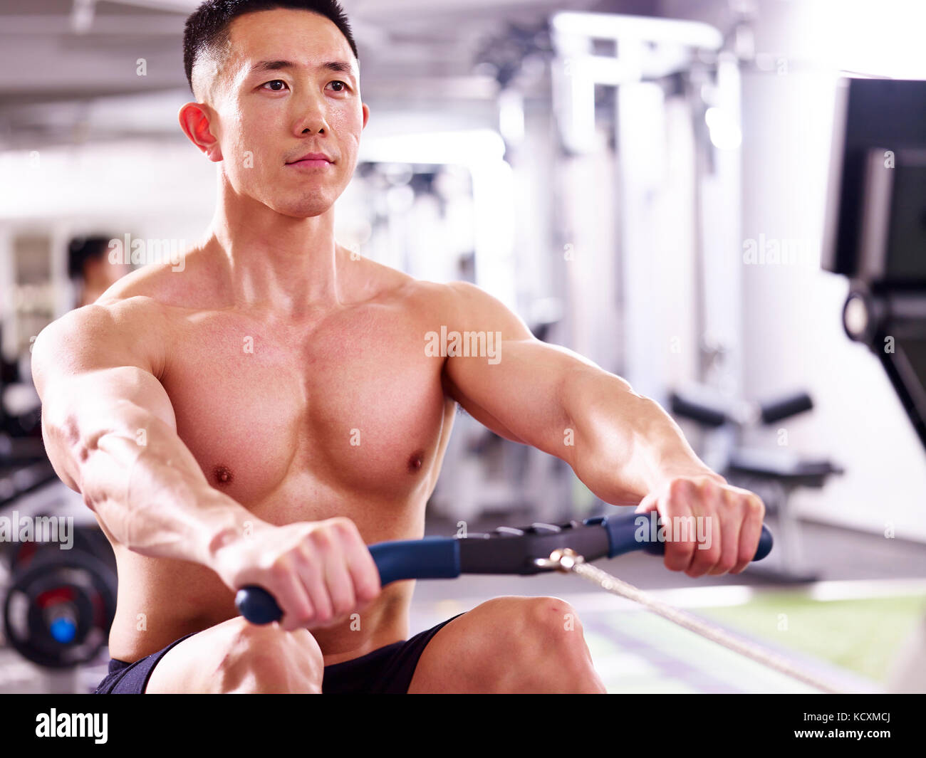 young asian muscle man working out in gym using rowing machine. Stock Photo