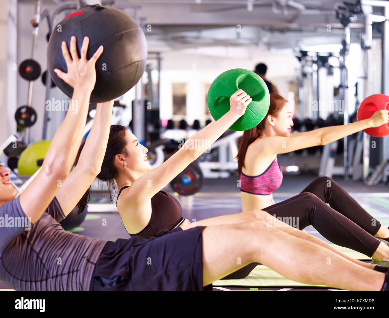 three young asian adult people working out in fitness center using medicine balls. Stock Photo