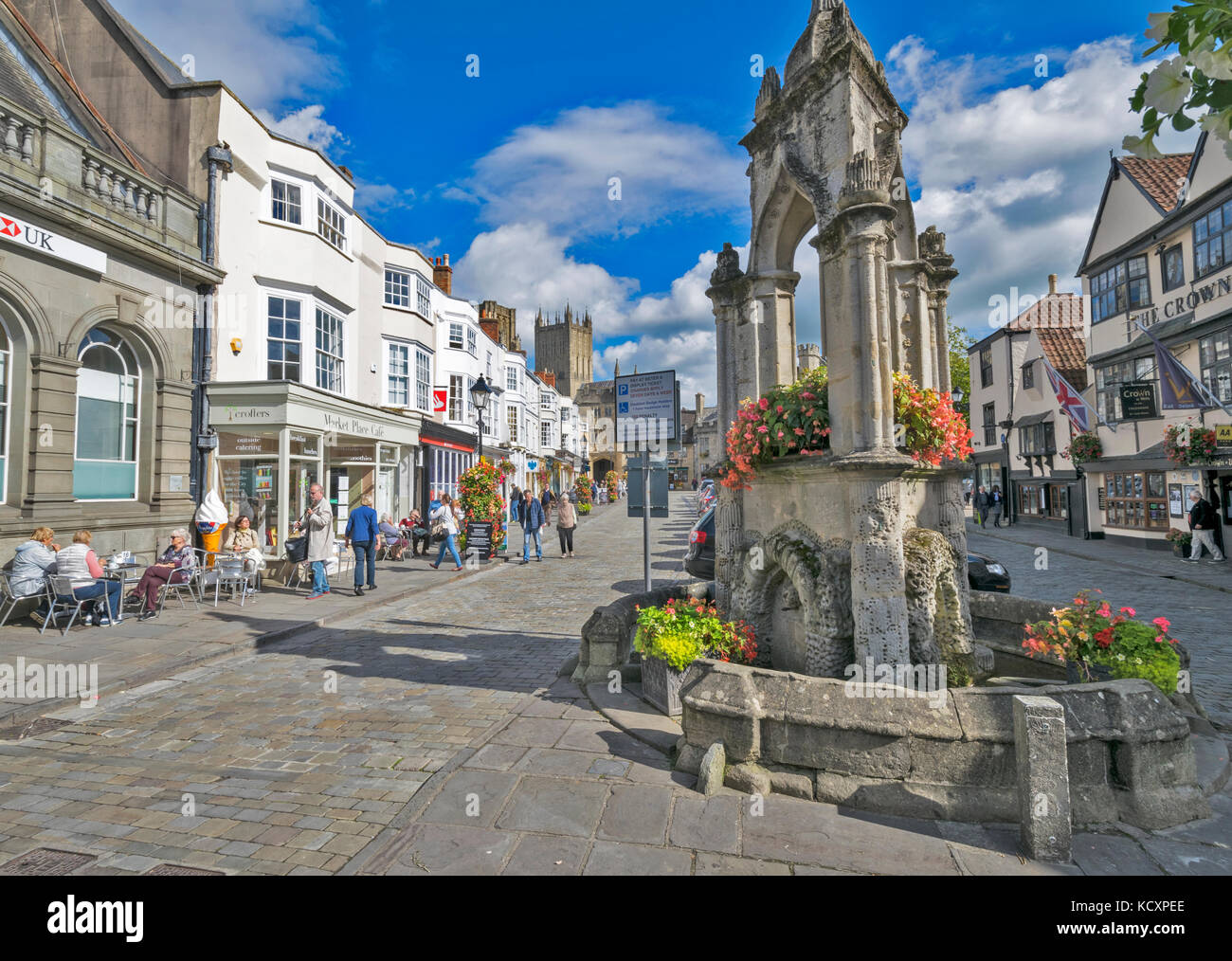 WELLS SOMERSET ENGLAND THE MAIN STREET LEADING TO THE CATHEDRAL AND ANCIENT FOUNTAIN WITH FLOWER DISPLAYS Stock Photo