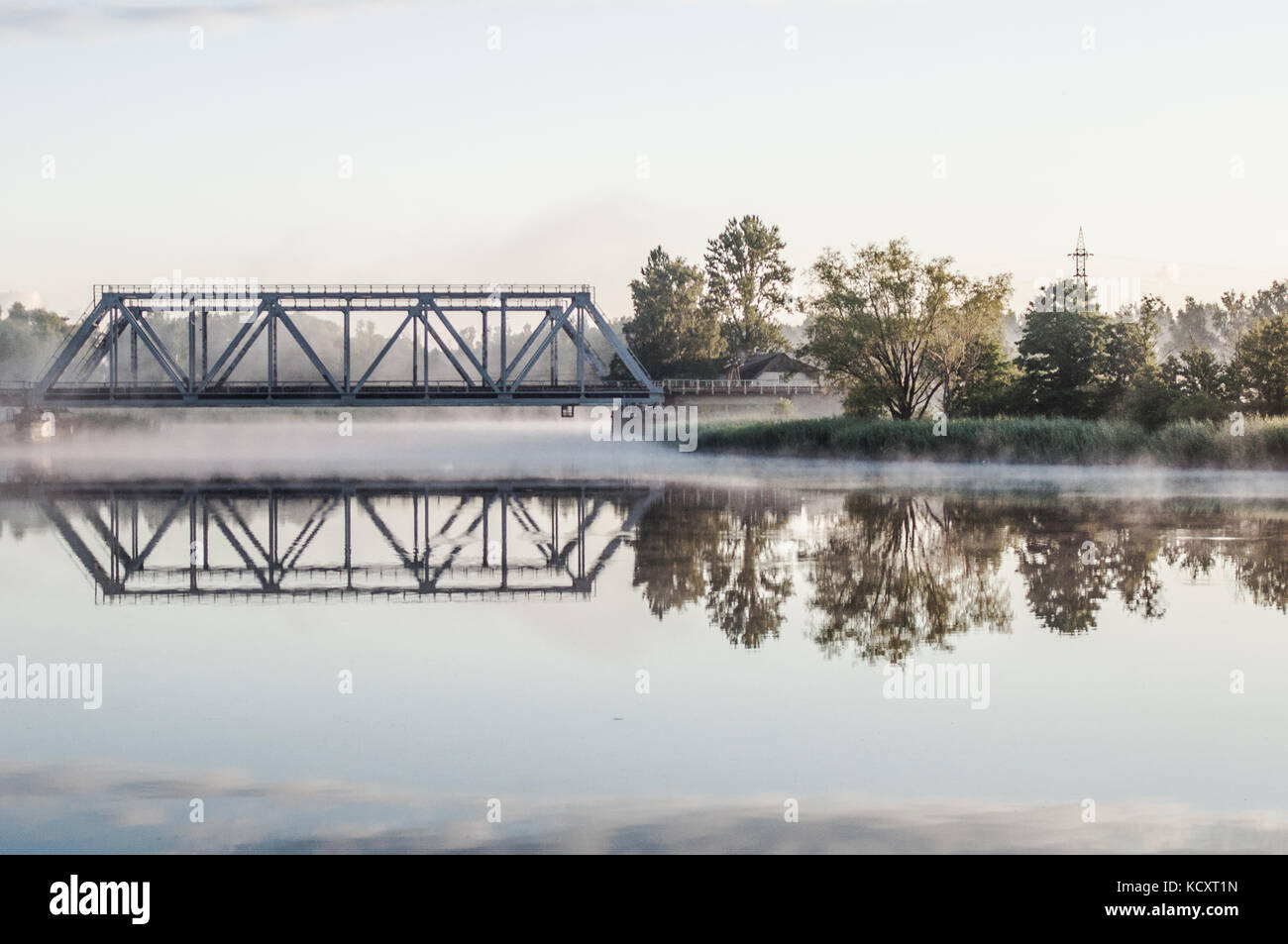 Railway bridge above misty lake. Reflection on water surface. Stock Photo