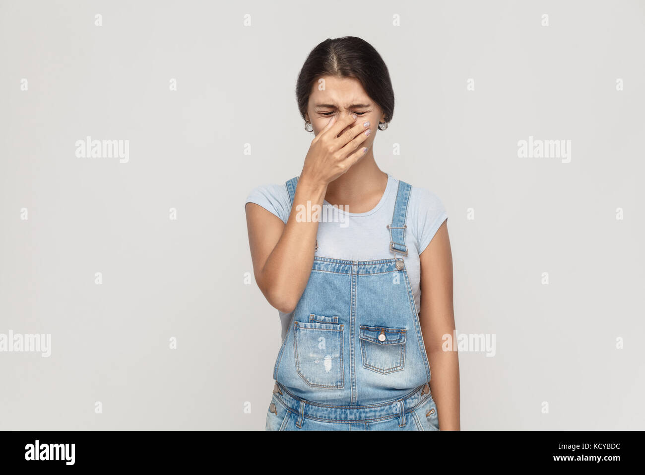 Unhappy and depressed young adult  gypsy woman, feeling ashamed or sick, covering face with both hands, keeping eyes closed. Isolated studio shot on g Stock Photo