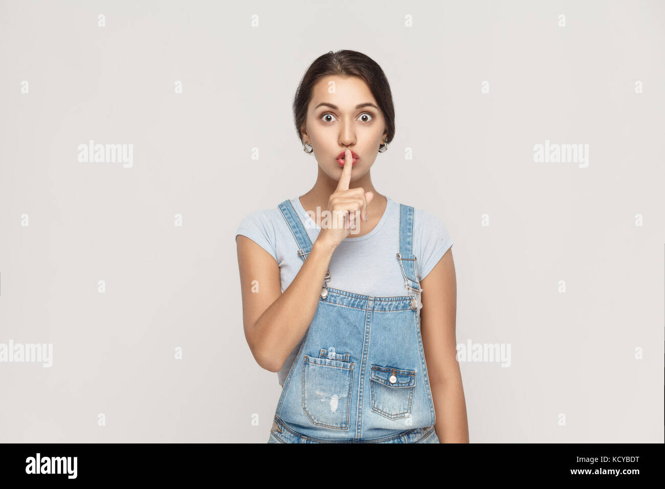 Shh sign. Beautiful indian woman looking at camera with silent sign. Studio shot, on gray background. Stock Photo