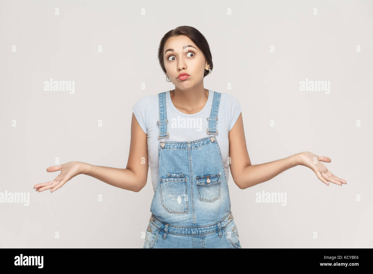 Negative human emotions, facial expressions. Puzzled  young adult woman with arms out, shrugging her shoulders, saying: who cares, so what, I don't kn Stock Photo