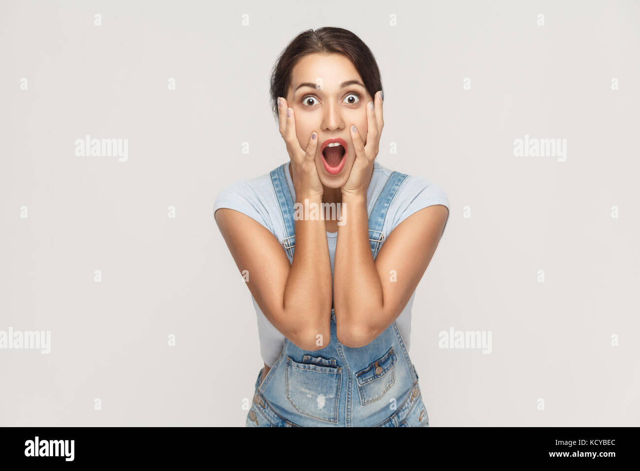 Human face expressions and emotions. Arab young adult woman holding arms on her cheeks and shocked. Isolated on gray background, studio shot Stock Photo