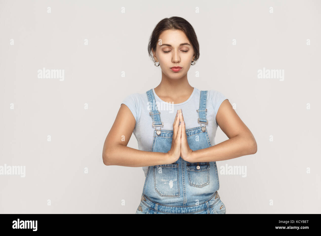 Beautiful young caucasian  female, holding hands in namaste or prayer, keeping eyes closed while practising yoga and meditating at home alone. Studio  Stock Photo
