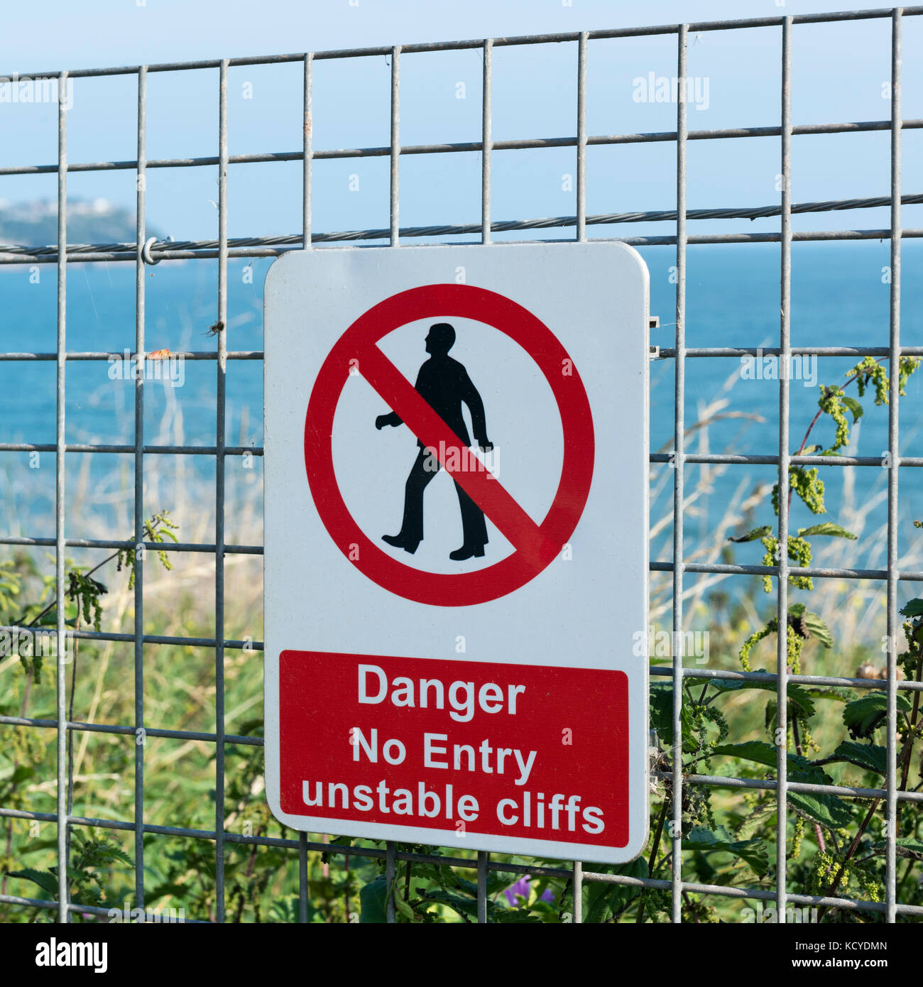 Black ,Red and White  Danger sign - No Entry unstable cliffs - on a wire fence  on the South West Coast Path near Paignton, Torbay Stock Photo