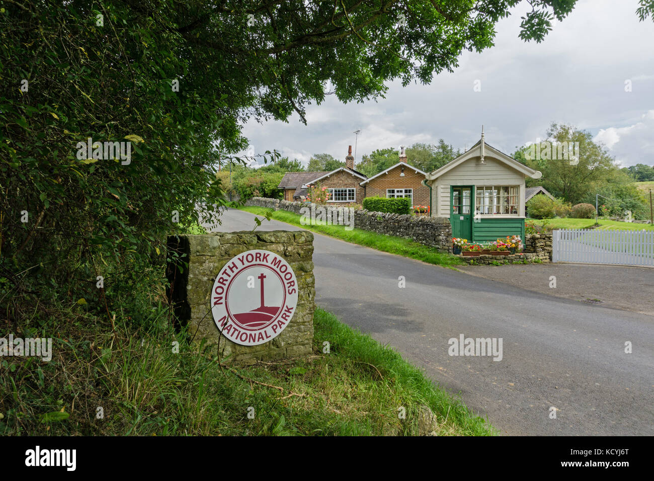 Circular sign for the North York Moors National Park, with an old railway signal box in the background; the village of Coxwold, North Yorkshire Stock Photo