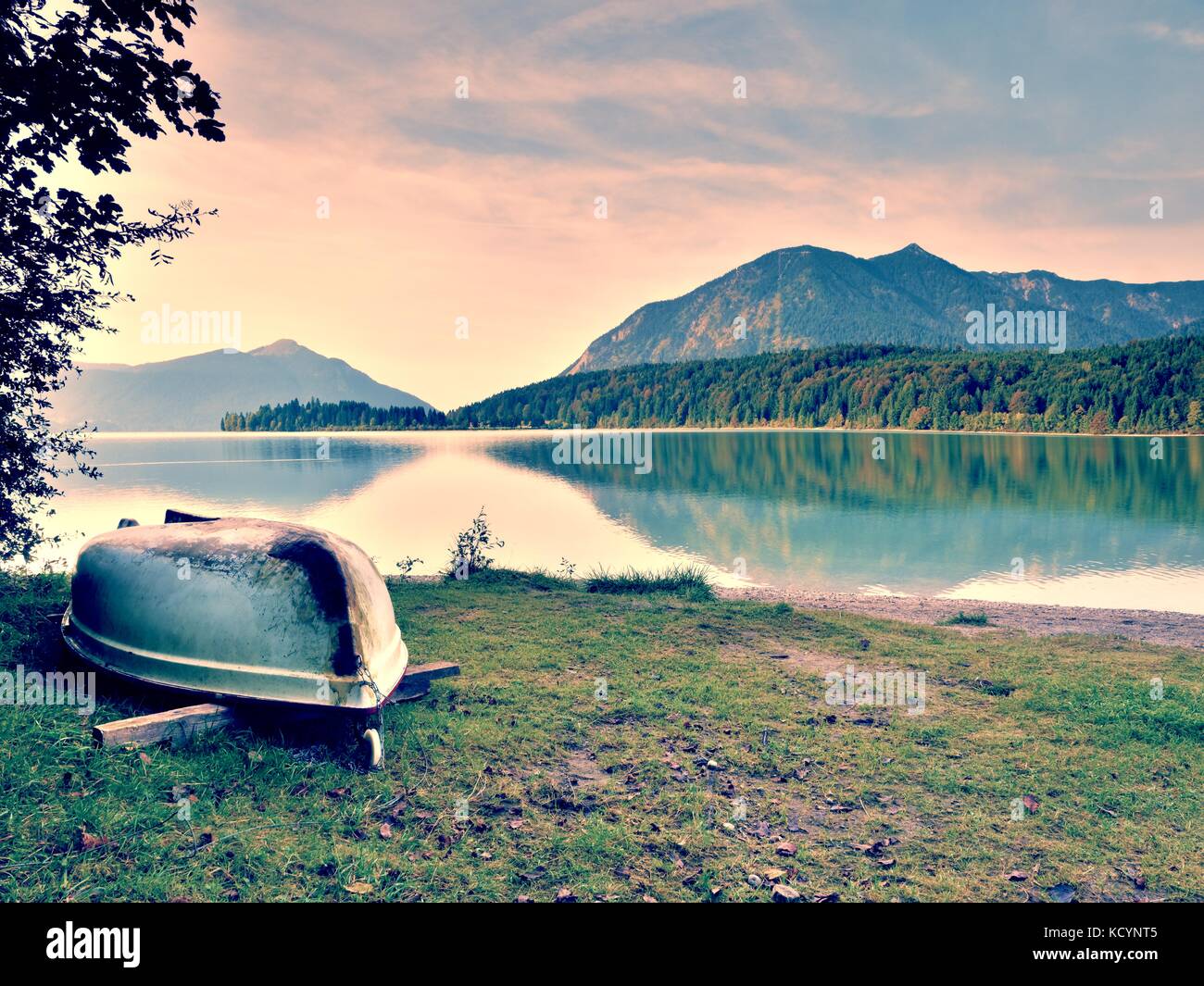 Upside down  fishing paddle boat on bank of Alps lake. Morning autumnal lake. Dramatic and picturesque scene. Mountains in water mirror. Stock Photo