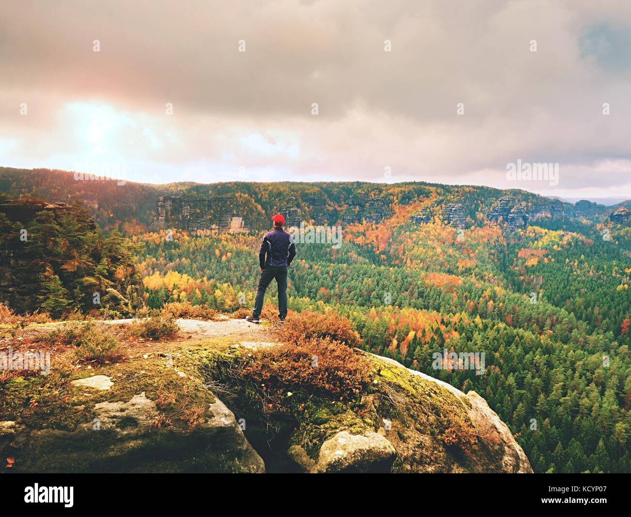 Alone tourist with outdoor sportswear and backpack stand on cliff edge  and watching into colorful autumn valley bellow.  Vintage Style Toned effect Stock Photo
