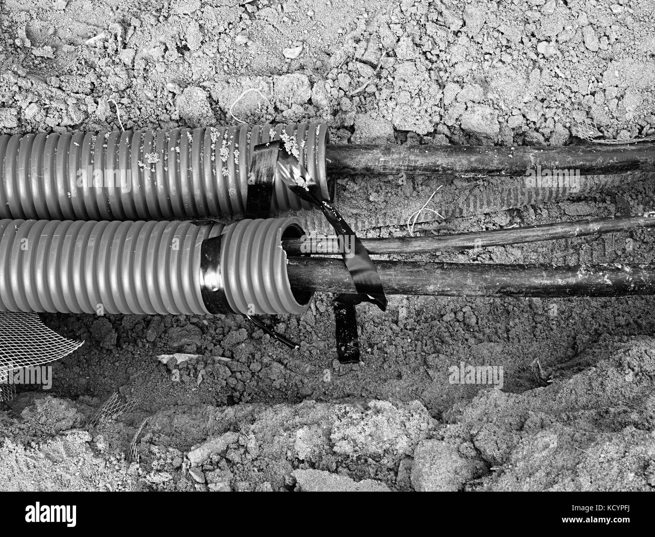 Excavation of trench  with black cables in protective HDPE tube. Lines of metallic and fiber optic cables, building of communication optical network.  Stock Photo