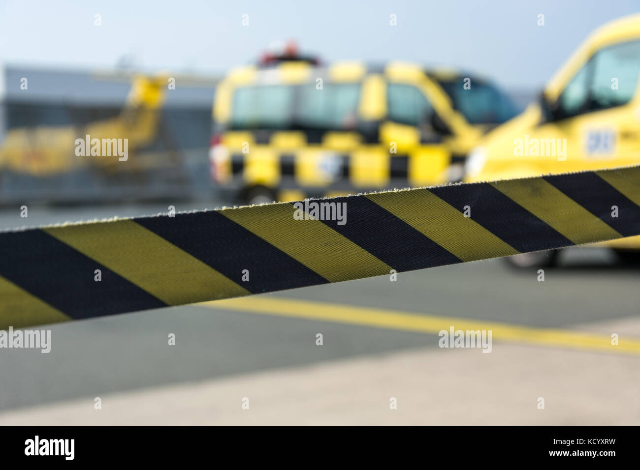 Black and yellow barrier tape at the airport with cars in the background Stock Photo