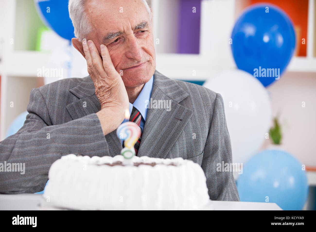 Sad senior man forgot how old is looking at birthday cake with a question mark Stock Photo