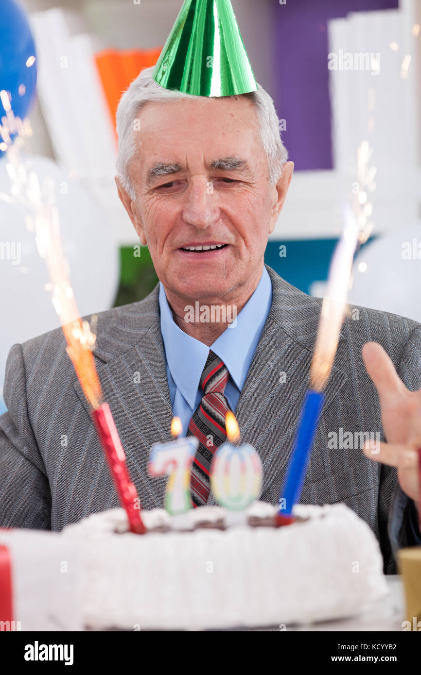Excited senior man looking at his birthday cake for 70th birthday Stock Photo