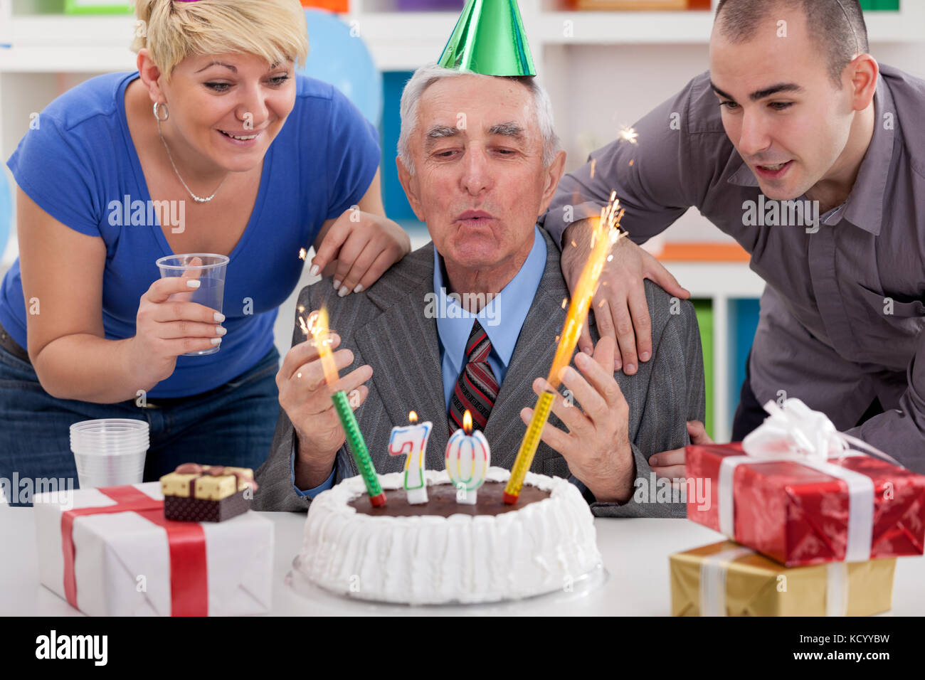 senior man blowing candles on birthday cake with family Stock Photo