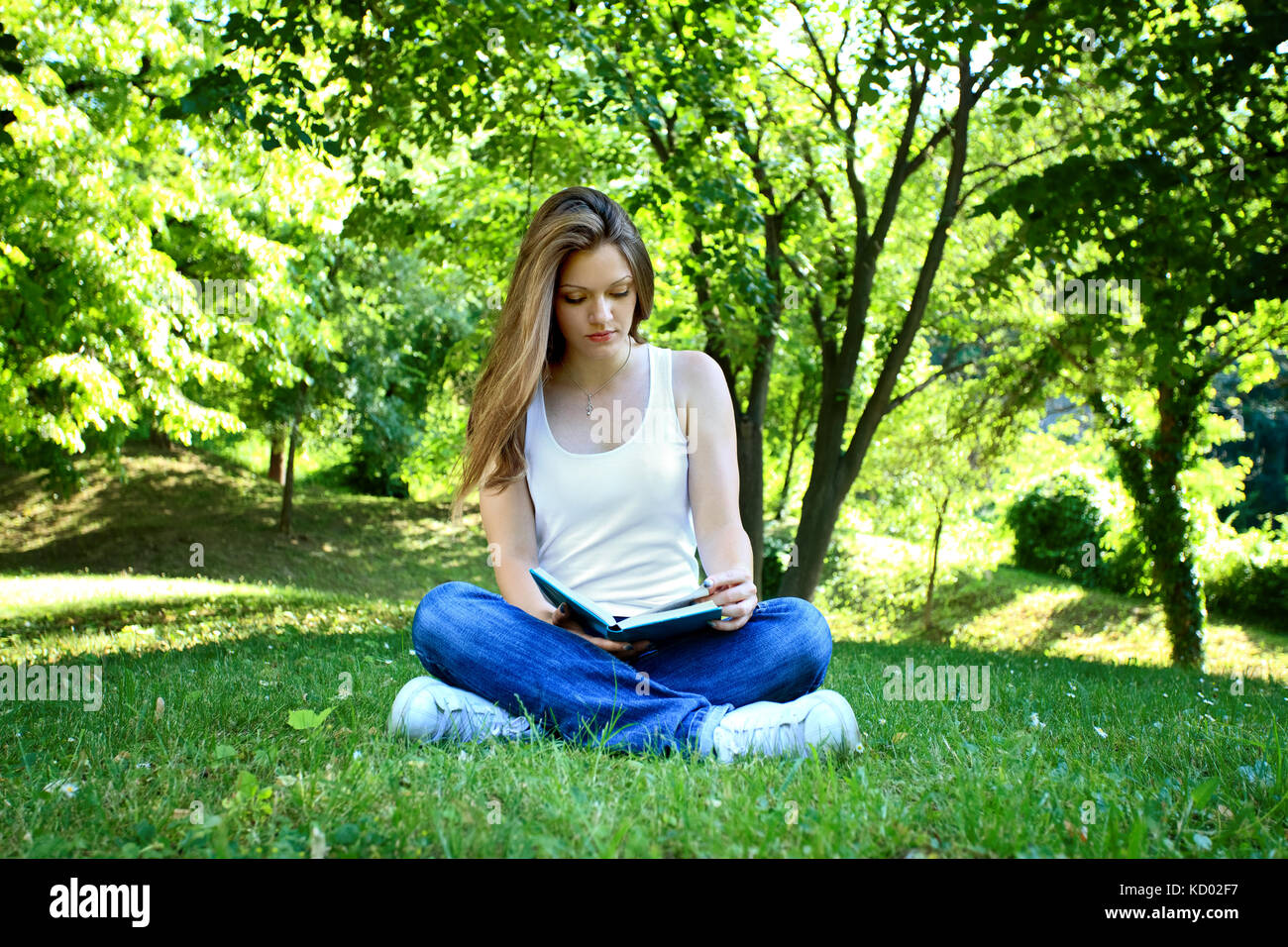 Young woman sitting in park and reading book Stock Photo - Alamy