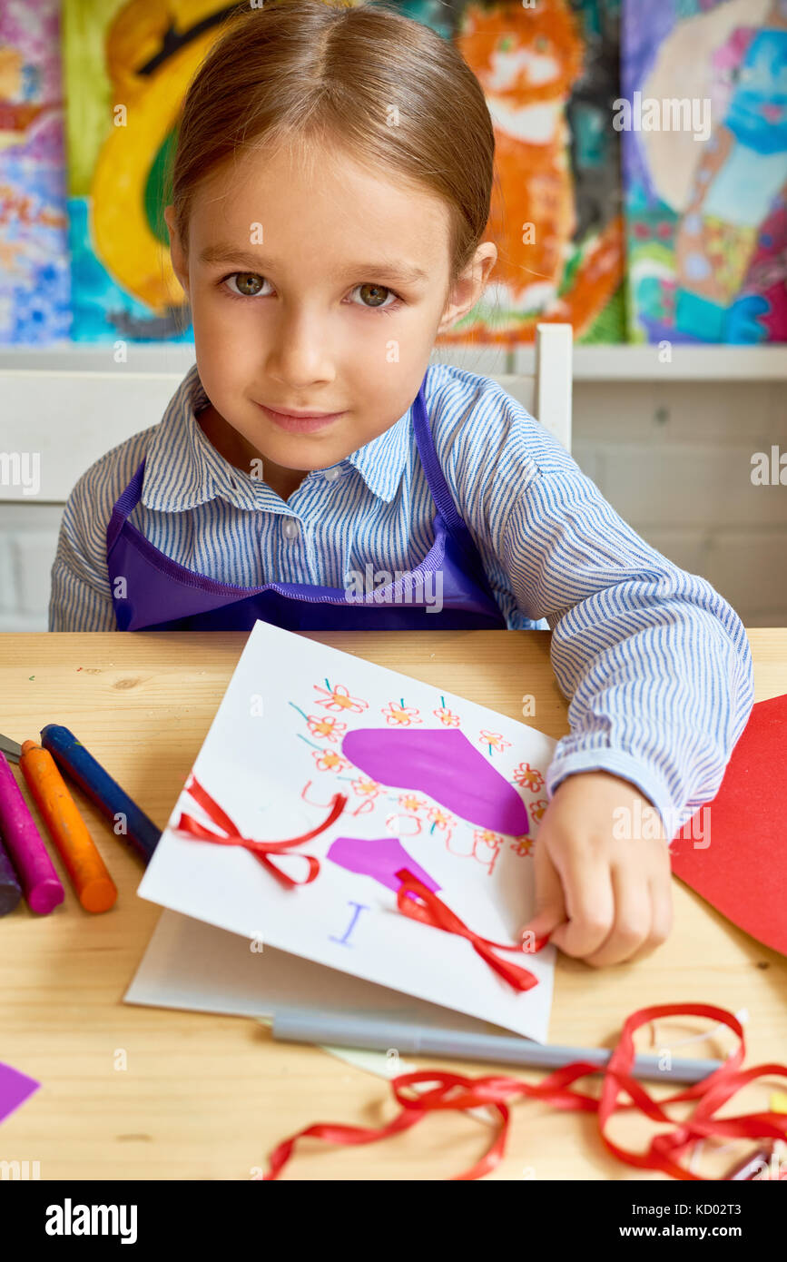 Portrait of adorable little girl looking at camera while making gift card for mom during art and craft class in pre-school Stock Photo