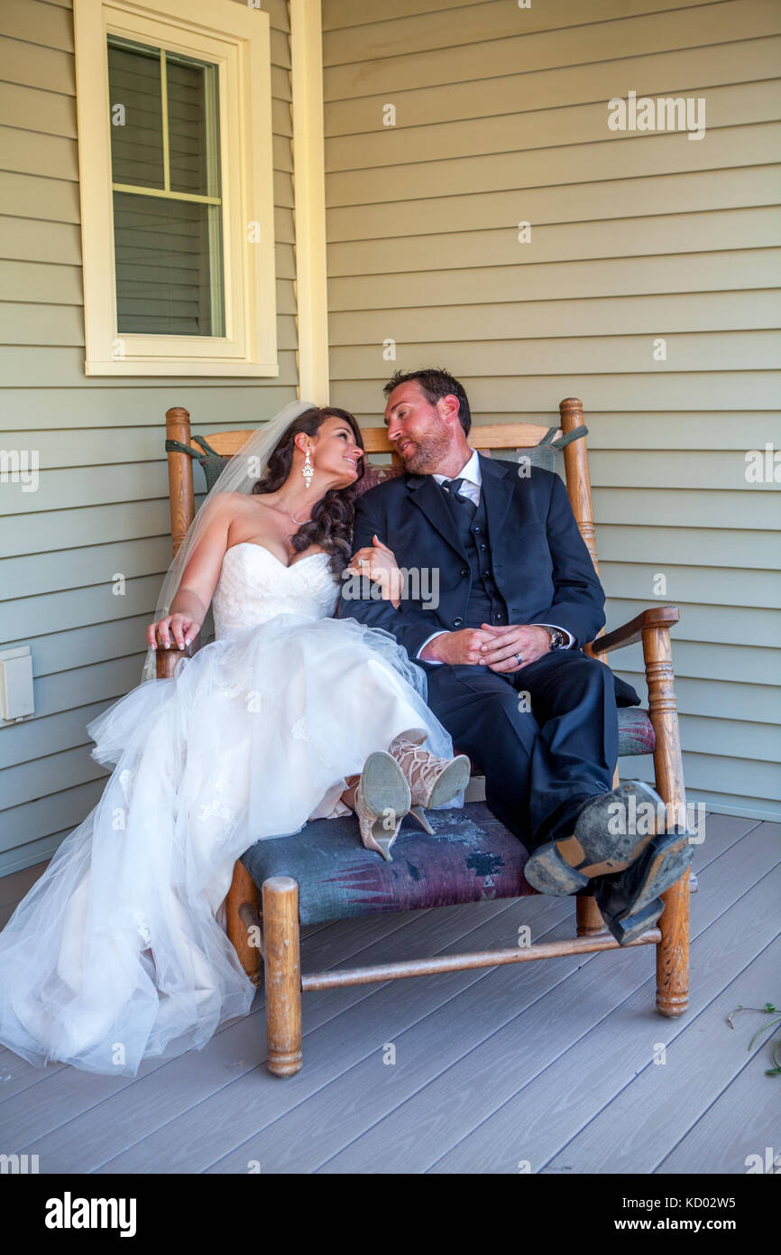 Newly married couple sit in a rocking chair wearing their tuxedo and wedding dress. Stock Photo