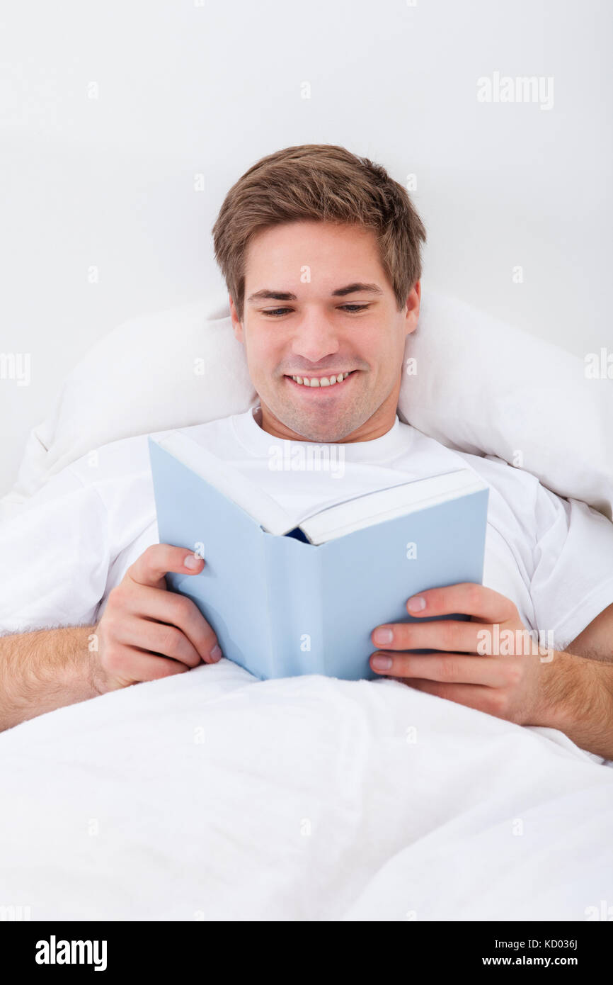 Happy Young Man Reading Book Lying On Bed Stock Photo