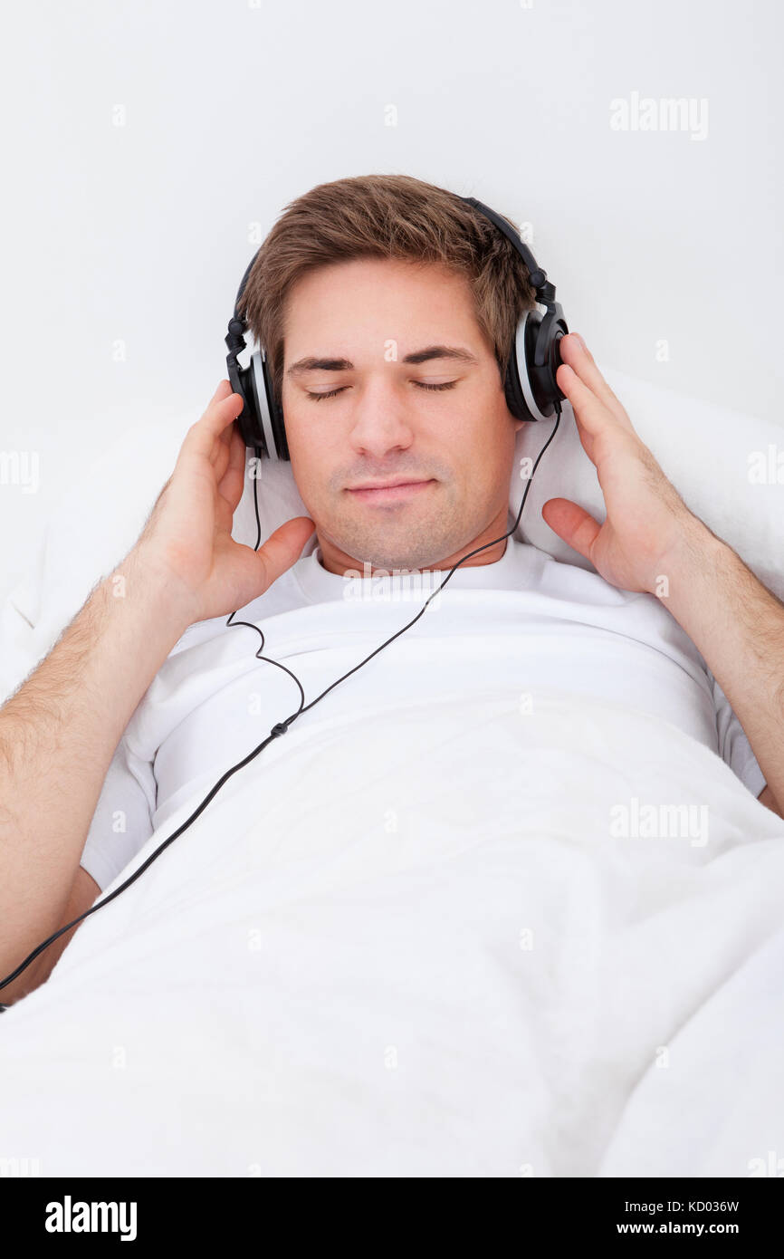 Young Man Lying On Bed Listening To Music With Headphones Stock Photo ...