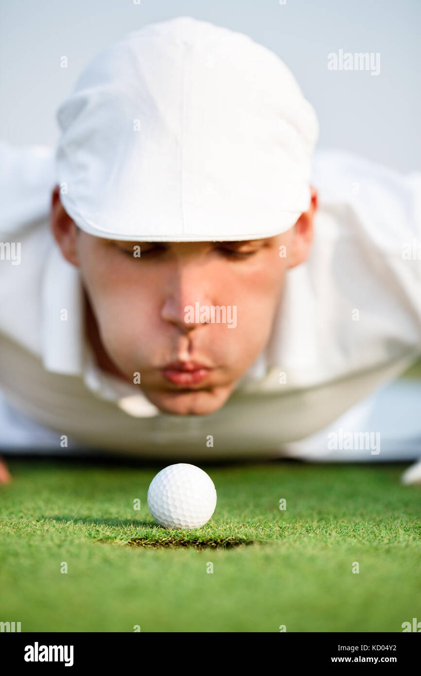 Desperate golfer blowing on golf ball to put in hole, funny golfing