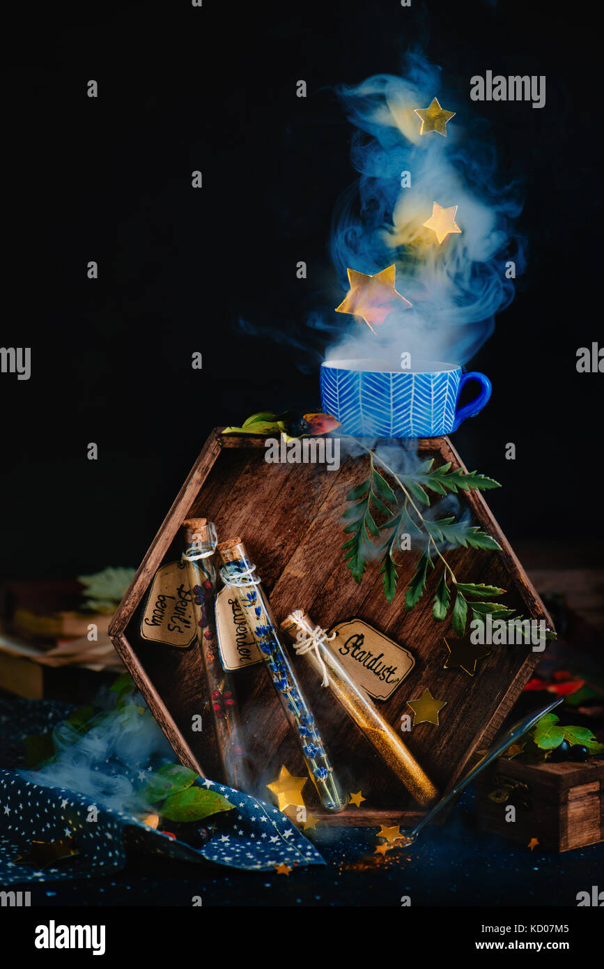 Test tubes with potion ingredients, lavender, berries, and stardust. Magical still life with staming cup of herbal tea, hexagonal wooden tray and dark Stock Photo