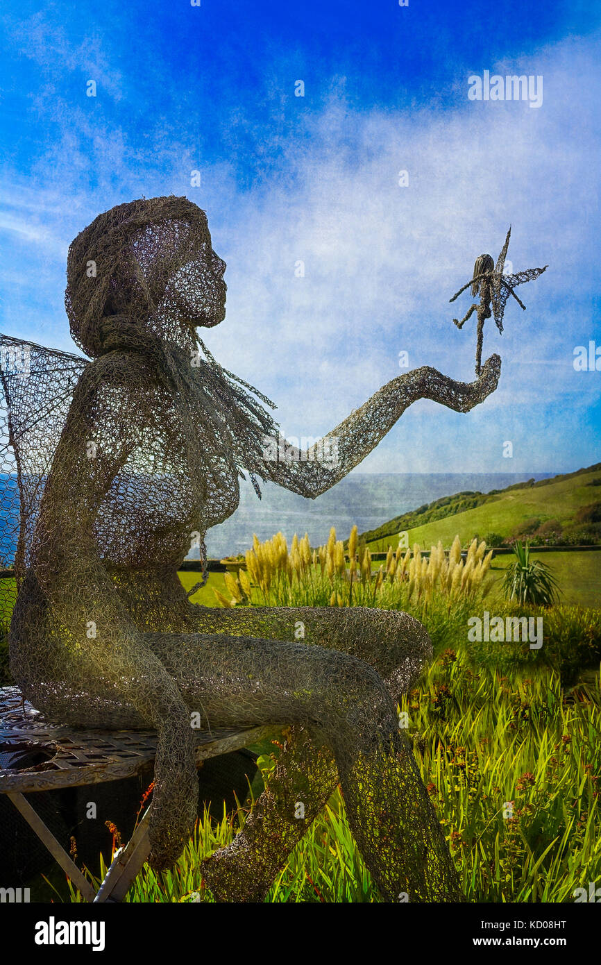 Life size wire sculpture by Derek Kinzett o a fairy queen holding a tiny fairy and is set against the backdrop of Talland Bay Cornwall Stock Photo