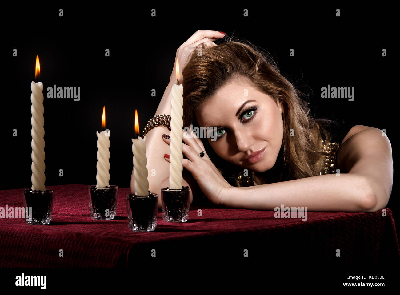 Beautiful young woman with bright green eyes near the candles over black background Stock Photo