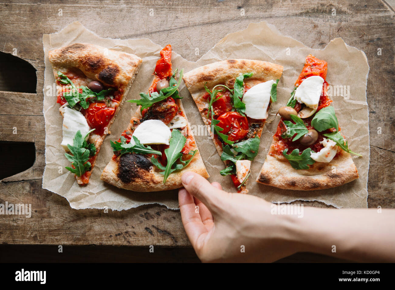 Woman taking pizza slice from chopping board, overhead view Stock Photo