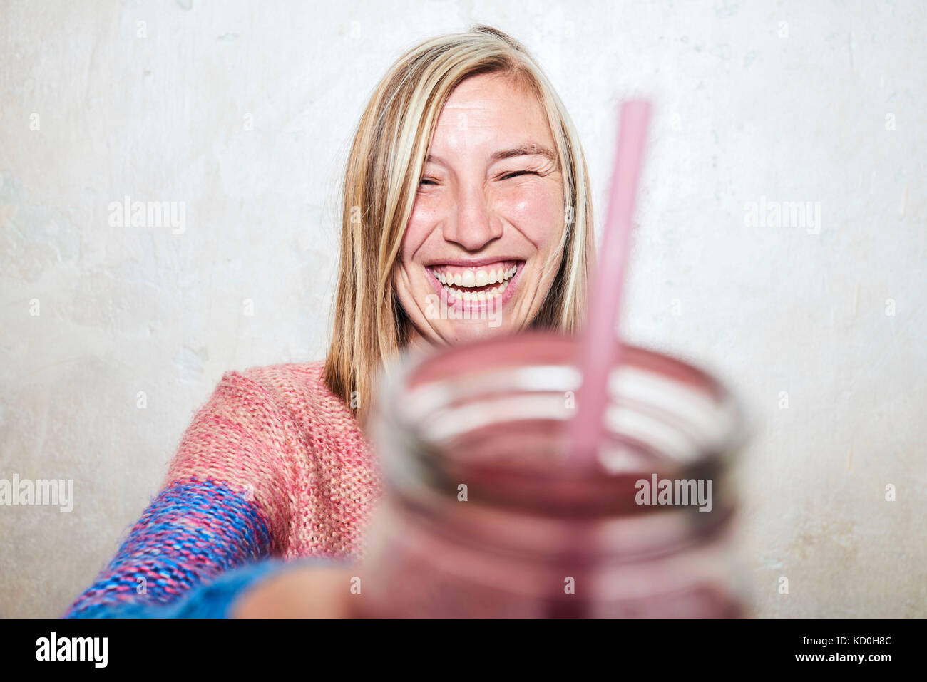 Portrait of woman holding drink towards camera, laughing Stock Photo