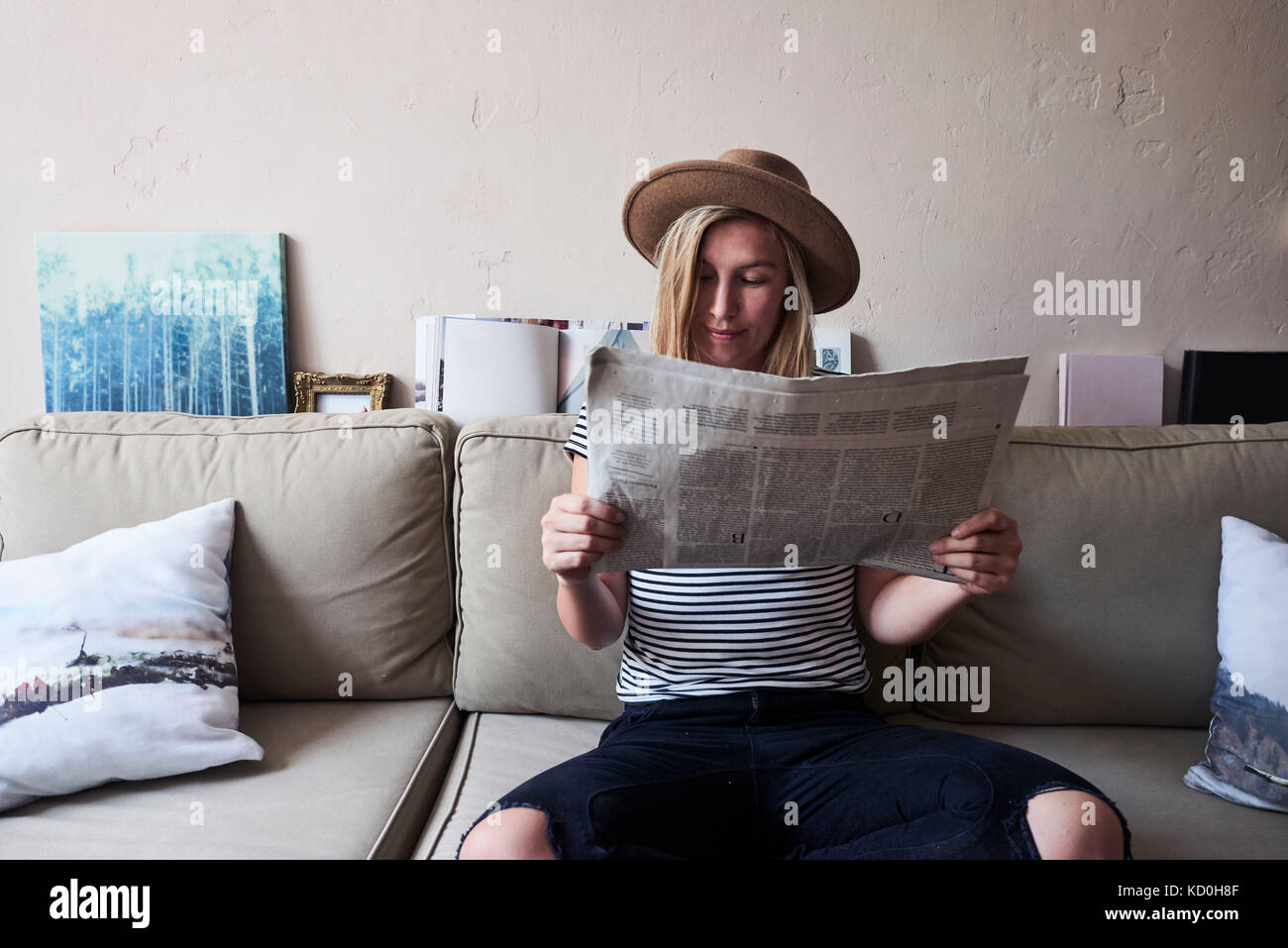 Woman sitting on sofa, reading newspaper Stock Photo