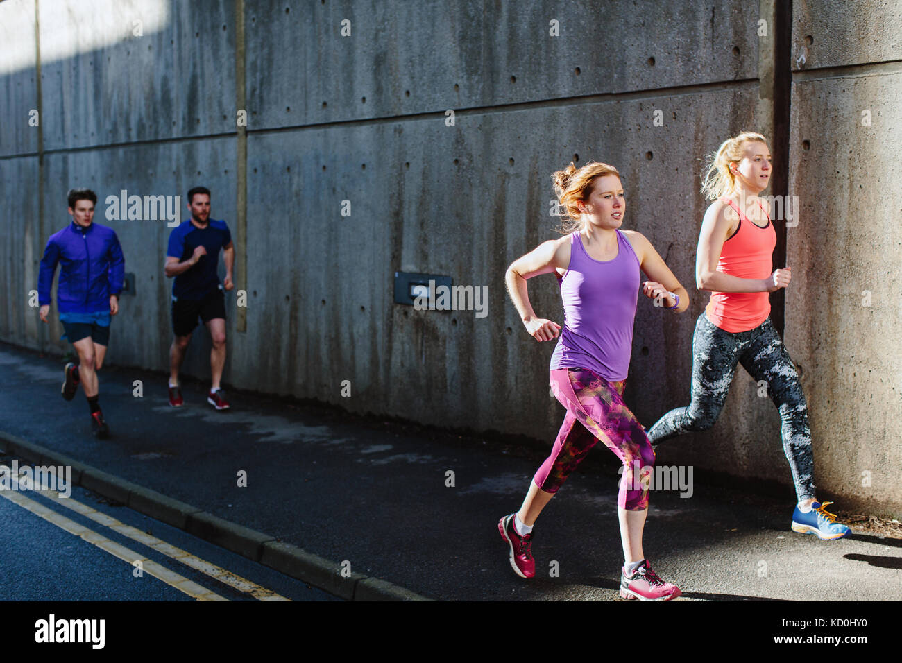 Four young adult runners running along city sidewalk Stock Photo - Alamy