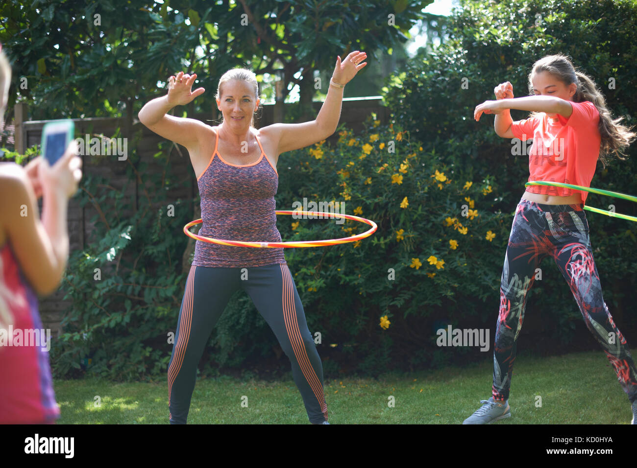 Girl photographing mother and teenage sister hoola hooping in garden Stock Photo