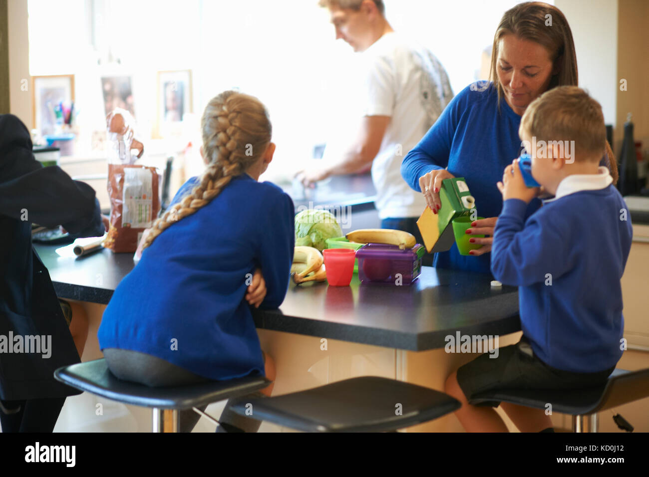 Mother pouring juice for her school children in kitchen Stock Photo
