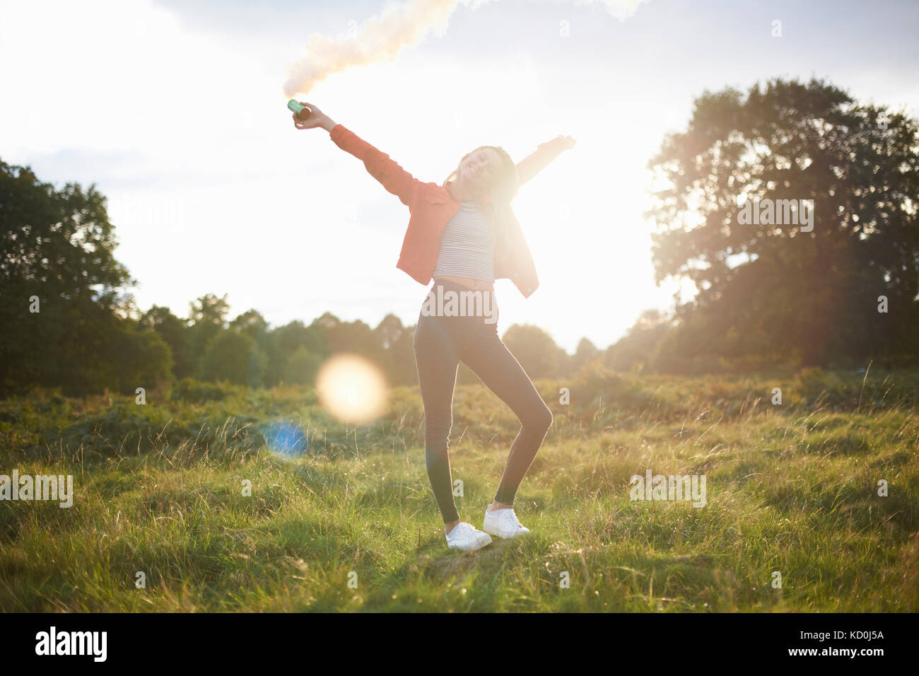 Young woman letting off smoke flare in sunlit field Stock Photo