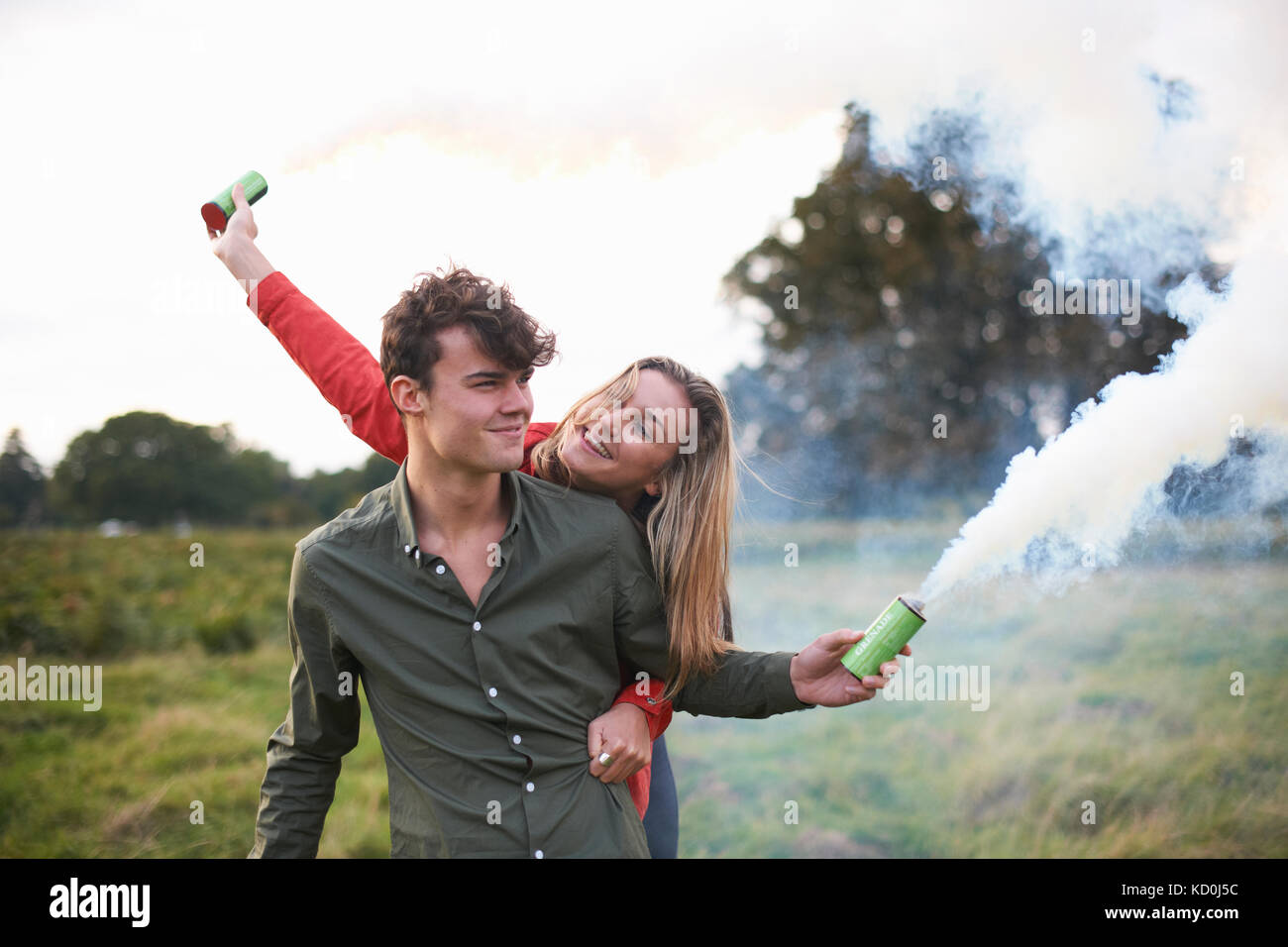 Young couple letting off smoke flares in field Stock Photo