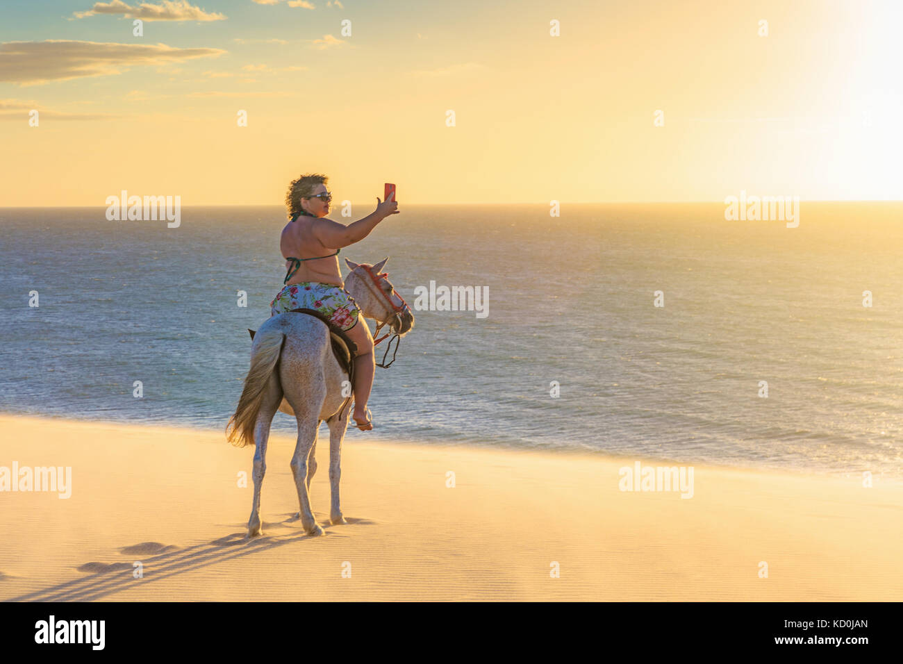 Woman riding horse on beach, taking picture of view using smartphone, Jericoacoara, Ceara, Brazil, South America Stock Photo