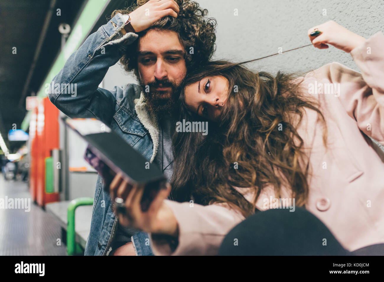 Young couple sitting in train station, looking at smartphone, worried expressions Stock Photo