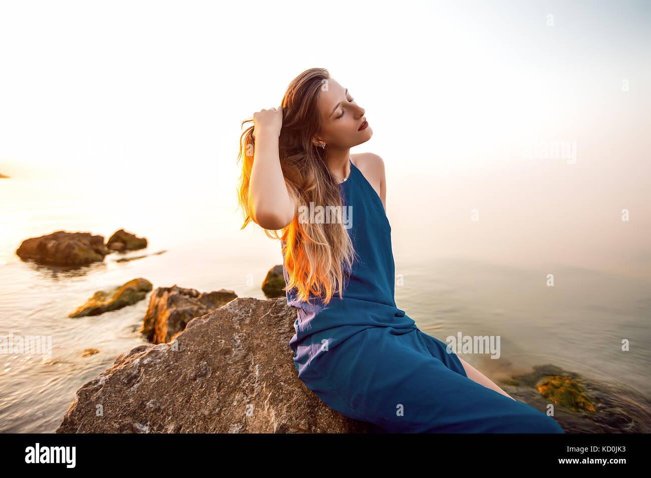 Young woman sitting on beach rock with hand in long hair, Odessa, Ukraine Stock Photo
