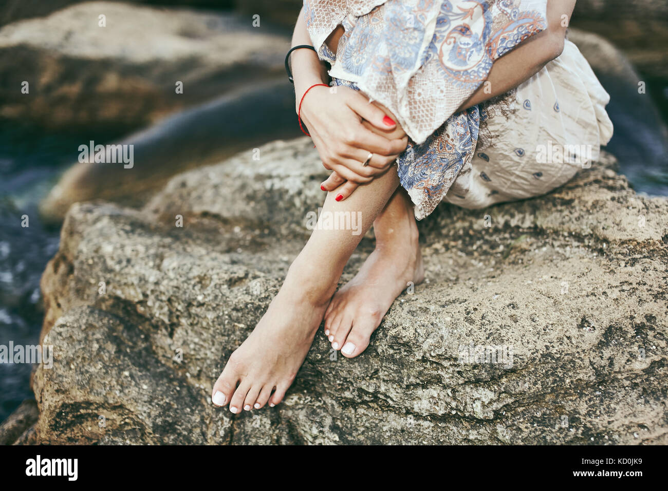 Waist down view of young woman sitting barefoot on coastal rock, Odessa, Ukraine Stock Photo