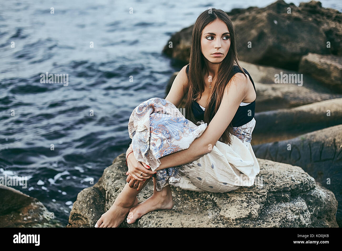 Young woman sitting on coastal rock looking over her shoulder, Odessa, Ukraine Stock Photo