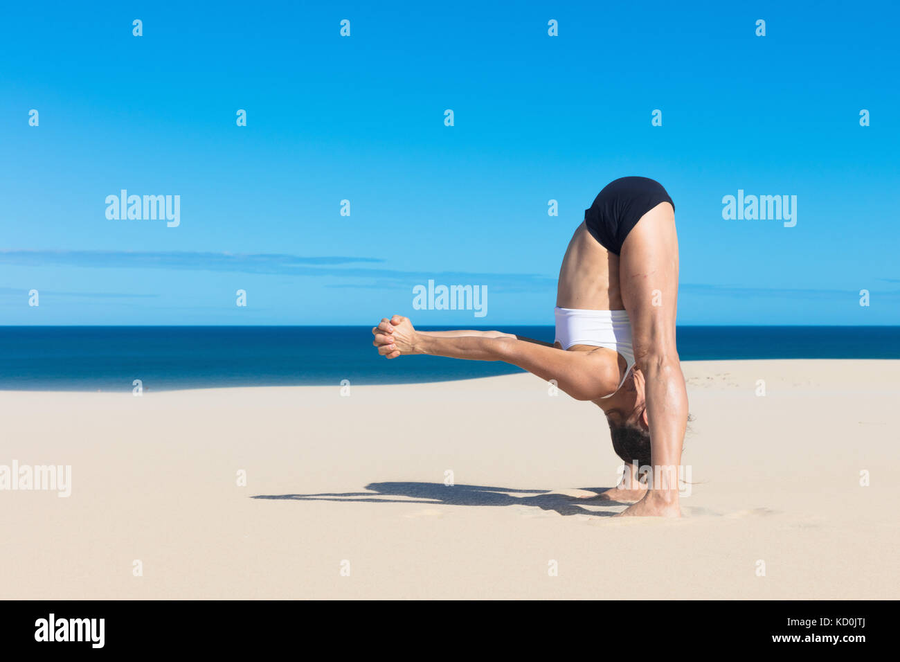 Side view of woman on beach bending forwards in yoga position Stock Photo